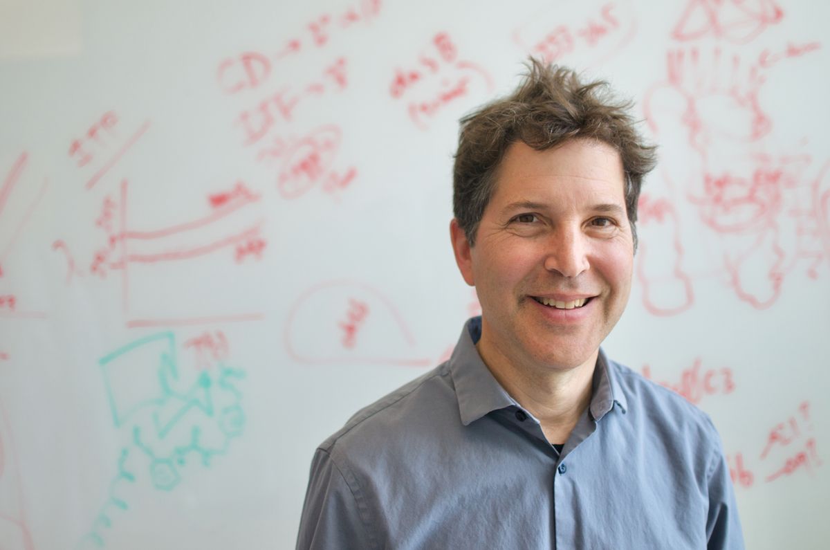 David Baker, wearing a blue shirt, stands against a whiteboard in the background.