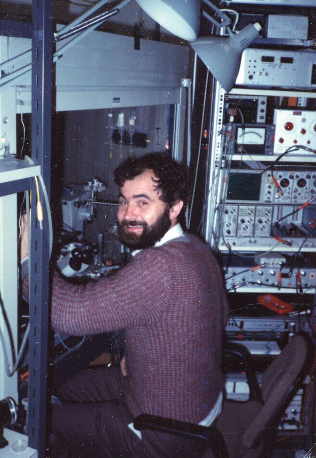 A man smiles back at the camera as he sits in front of a fume hood.