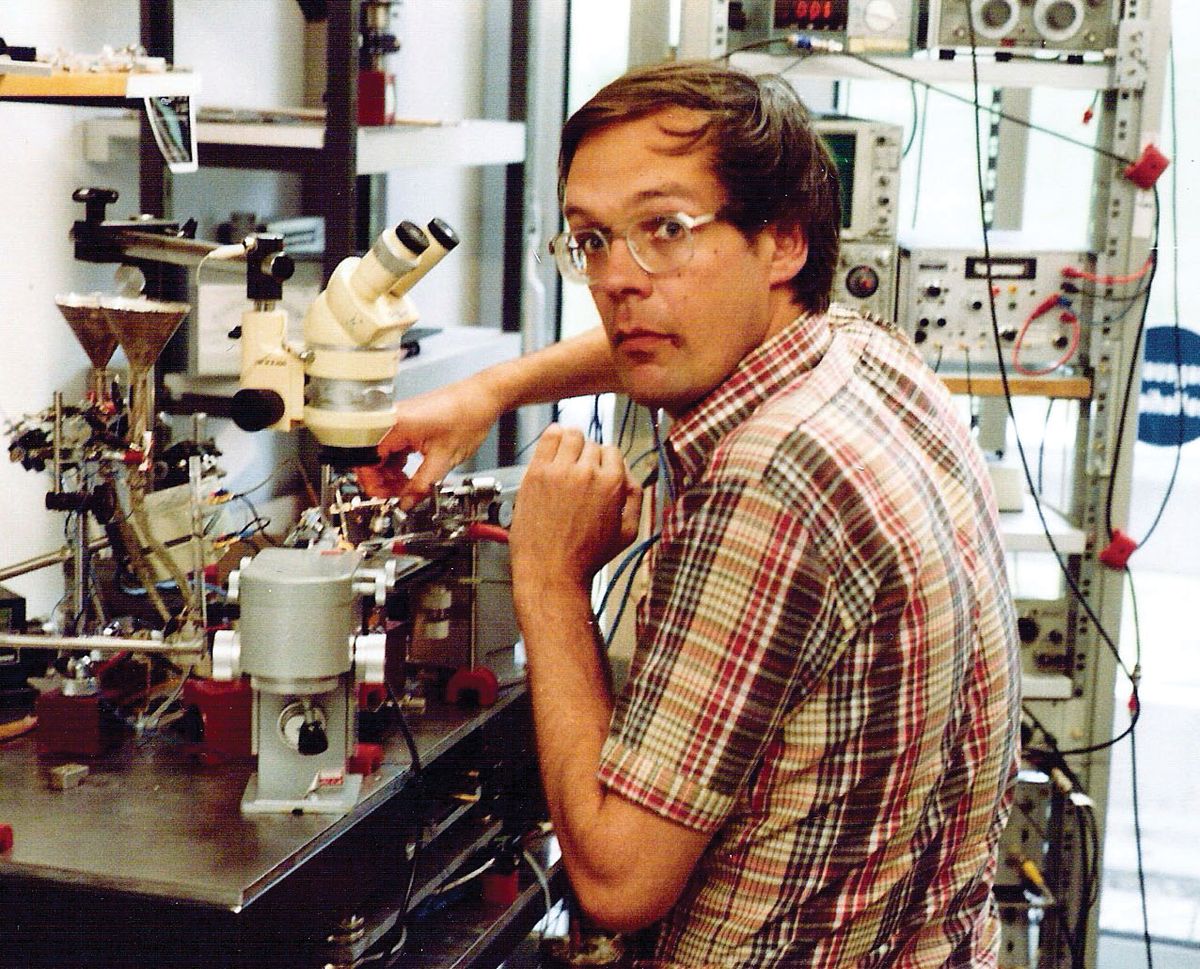 A man stands in front of a microscope setup.