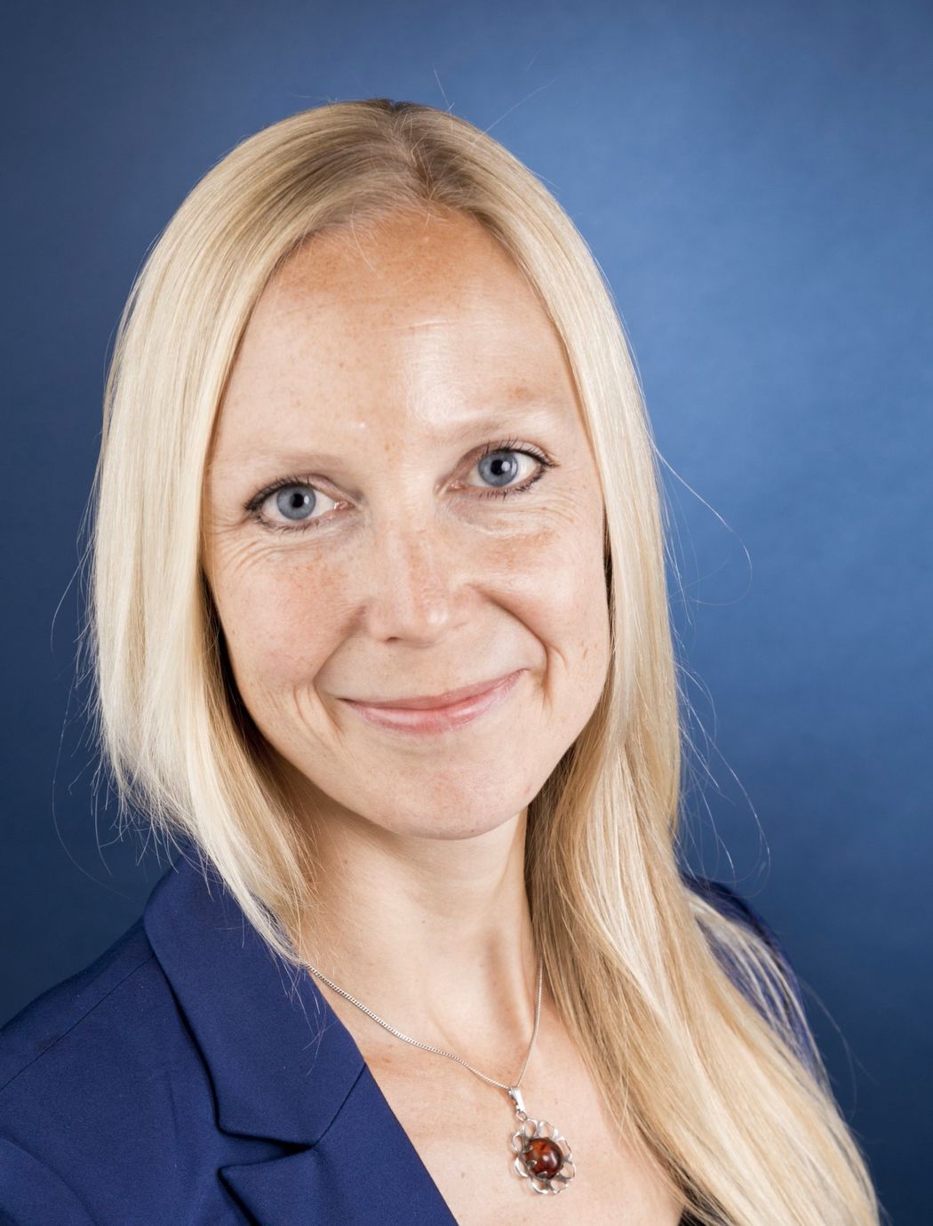 Virologist Gisa Gerold smiles at the camera. She is wearing a blue blazer and is standing against a blue background.