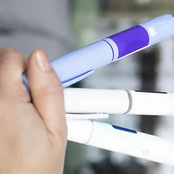 A hand holding multiple injection pens.