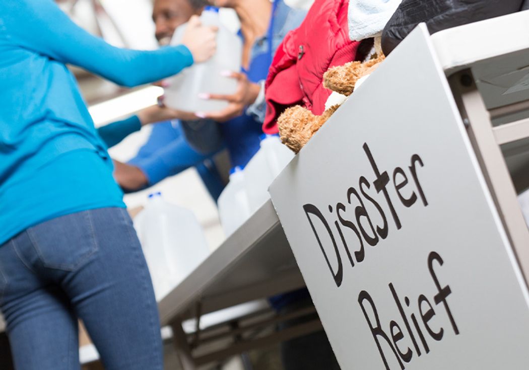 A photograph showing a sign that reads “Disaster Relief” at a table handing out water to people.