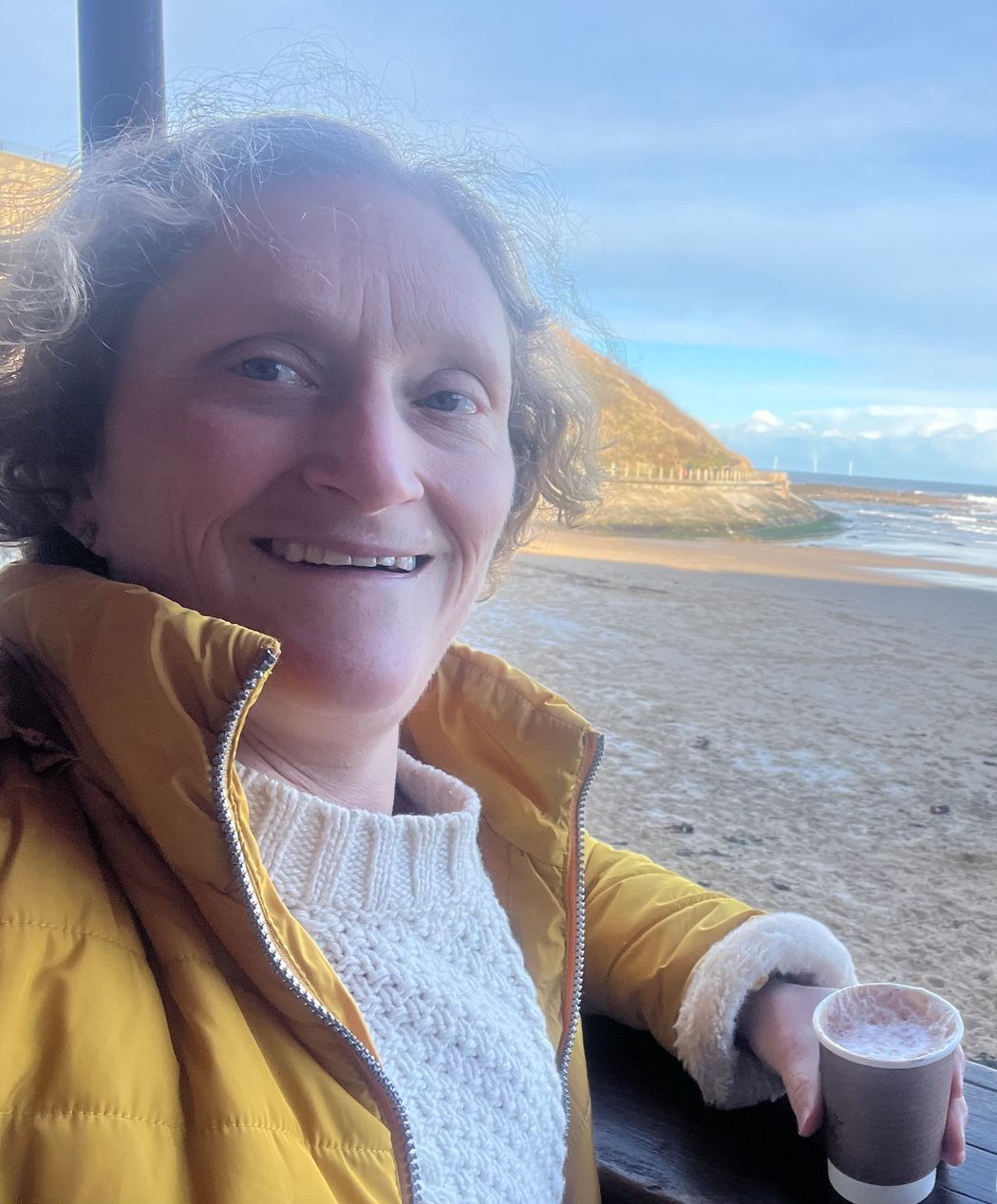 Joanna Elson’s selfie in front of a beach at Newcastle. She’s wearing a white sweater, yellow jacket, and is holding a cup of coffee. Joanna Elson’s selfie in front of a beach at Newcastle. She’s wearing a white sweater, yellow jacket, and is holding a cup of coffee.