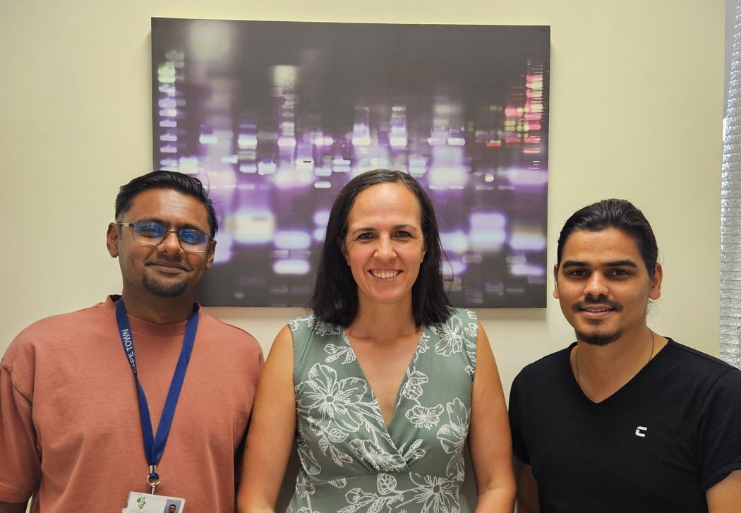 Surita Meldau, wearing a green top, stands in the center surrounded by Shrinav Dawlat wearing an orange T-shirt on the left and Kashief Khan wearing a black T-shirt on the right. All three of them smile at the camera. Surita Meldau, wearing a green top, stands in the center surrounded by Shrinav Dawlat wearing an orange T-shirt on the left and Kashief Khan wearing a black T-shirt on the right. All three of them smile at the camera.