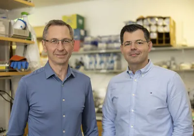 Petros Giannikopoulos (right) and Fyodor Urnov (left) stand in the lab where the on-demand CRISPR therapy was produced. They are both wearing blue shirts and glasses. 