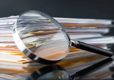 A photo showing a stack of papers and a magnifying glass