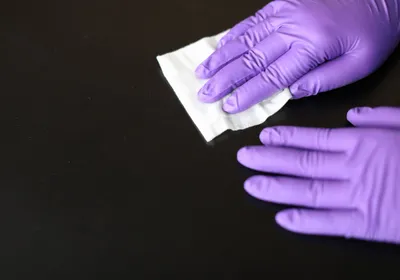 Scientist wearing purple nitrile gloves and cleaning a surface with a disinfectant wipe