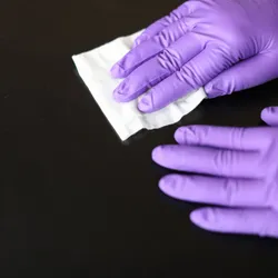 Scientist wearing purple nitrile gloves and cleaning a surface with a disinfectant wipe