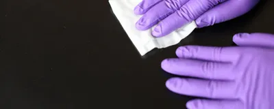Scientist wearing purple nitrile gloves and cleaning a surface with a disinfectant wipe