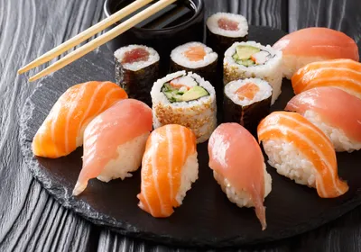Image of salmon and tuna nigiri as well as California rolls arranged on a circular black plate. Image of salmon and tuna nigiri as well as California rolls arranged on a circular black plate.