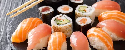Image of salmon and tuna nigiri as well as California rolls arranged on a circular black plate.