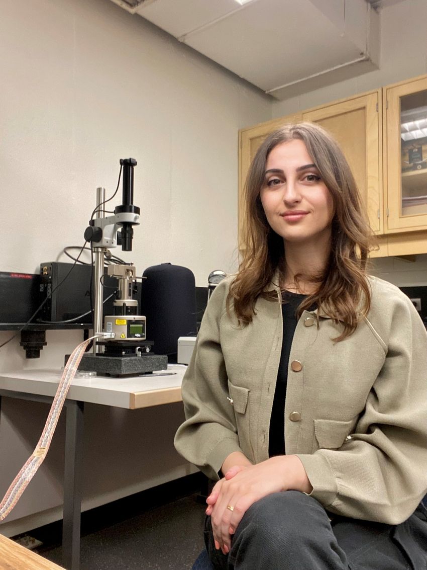 Image of Alaa Al-Shaer sitting beside a microscope setup. Image of Alaa Al-Shaer sitting beside a microscope setup.