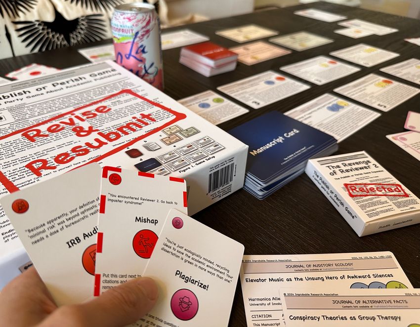 Image of a hand holding up three playing cards. The background has multiple cards set up on a wooden table. Image of a hand holding up three playing cards. The background has multiple cards set up on a wooden table.