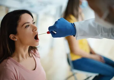 Doctor taking throat swab test from young female patient in the medical clinic. 