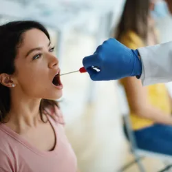 Doctor taking throat swab test from young female patient in the medical clinic. 