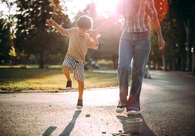 A boy holds his mom’s hand while playing hopscotch in the park.