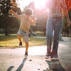 A boy holds his mom’s hand while playing hopscotch in the park.