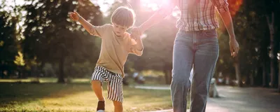 A boy holds his mom’s hand while playing hopscotch in the park.
