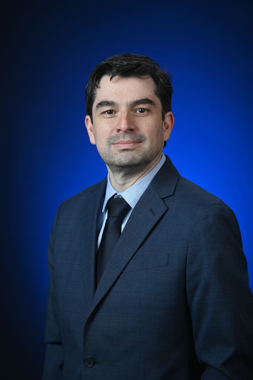 Image of Vitor Pomin, wearing a dark patterned suit, on dark blue background. Image of Vitor Pomin, wearing a dark patterned suit, on dark blue background.
