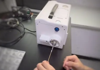 A person’s left hand holding cotton bud in front of a tabletop equipment.