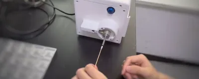 A person’s left hand holding cotton bud in front of a tabletop equipment.