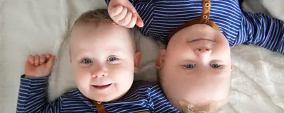 Identical twins lying upside down on white blanket.