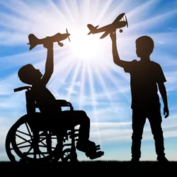 The silhouettes of two children, one standing and one in a wheelchair, playing with toy aeroplanes against a sunny blue sky.