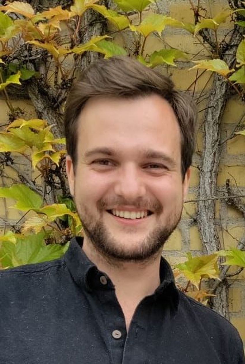 Image of Timothy Jenkins, wearing a dark polo shirt, in front of plants and a yellow brick wall. Image of Timothy Jenkins, wearing a dark polo shirt, in front of plants and a yellow brick wall.