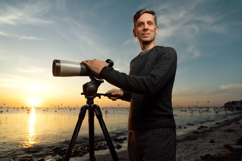 Jay Bolden stands on the shore of a beach at sunset with his hand on a scope. Jay Bolden stands on the shore of a beach at sunset with his hand on a scope.