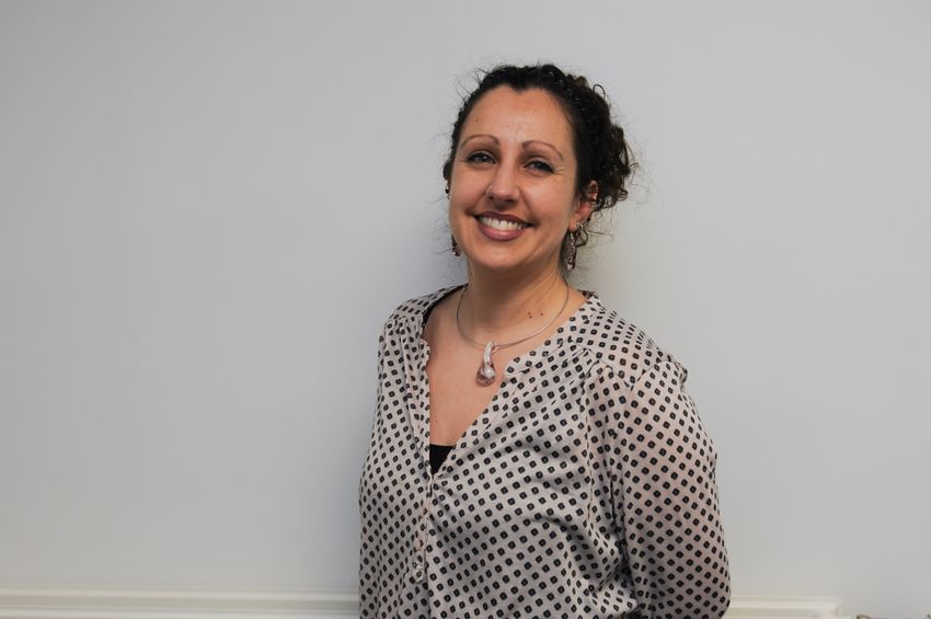 Caroline Horton wears a beige and black top and smiles at the camera against a white background.