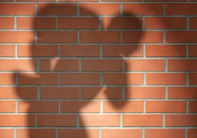 Spotlighted shadow of a robber-like figure on a brick wall. 