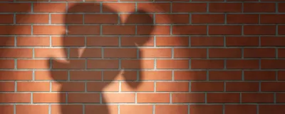 Spotlighted shadow of a robber-like figure on a brick wall.