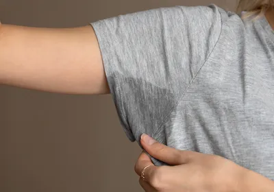 Image of a person in a gray shirt with a sweat stain in the armpit area of their shirt.