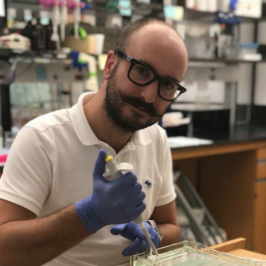 Simon Grelet holds a pipette in a gel box in front of a blurred background of a laboratory. He Simon Grelet holds a pipette in a gel box in front of a blurred background of a laboratory. He