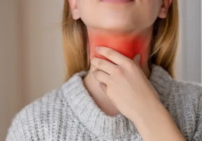 A girl holds her throat with her left hand. The region where the vocal cords would be is glowing red, indicating some strain, or even voice box cancer, which an AI-based tool may help detect. 