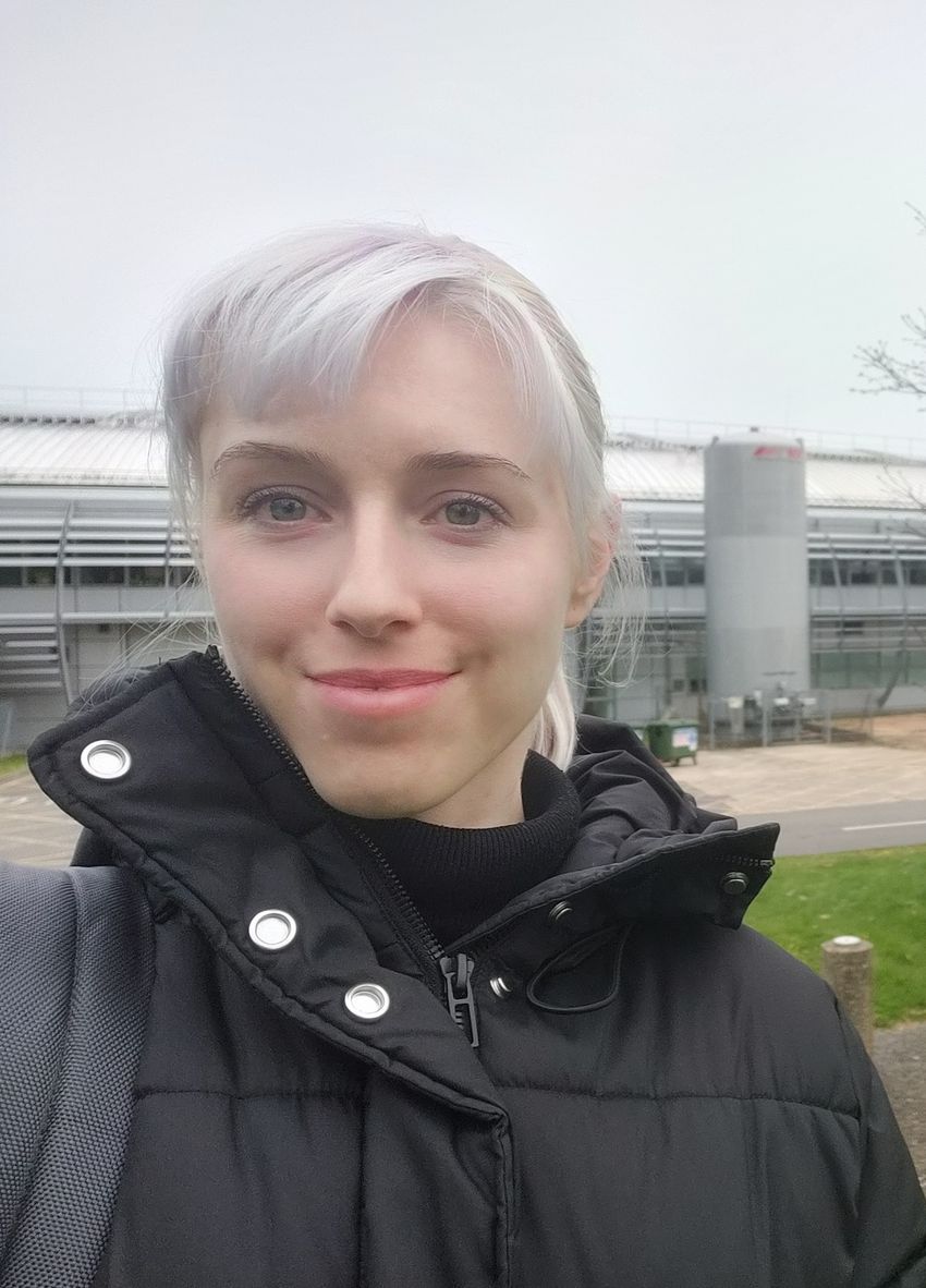 Selfie image of Esther González-Almela, wearing a black turtleneck sweater under a black winter jacket, in front of a building. Selfie image of Esther González-Almela, wearing a black turtleneck sweater under a black winter jacket, in front of a building.