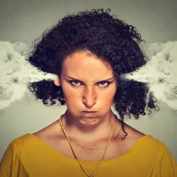 A closeup picture of an angry woman, with steam blowing out of her ears. She wears a yellow top and growls at the camera. 