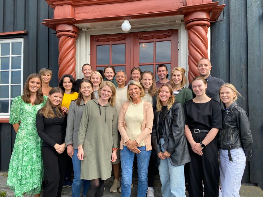 Several fetal microchimerism researchers pose for a picture outdoors in front of a painted wooden building.