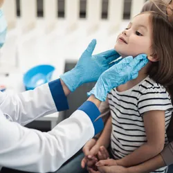 A doctor examines tonsils of a smiling little girl sitting in a woman’s lap.