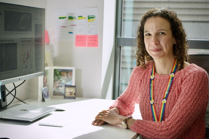 Maria Duque-Correa wears a pink sweater and sits at her desk with her hands folded.