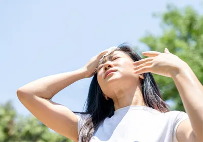 An Asian woman wiping sweat from her face on a hot day.