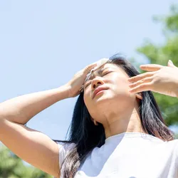 An Asian woman wiping sweat from her face on a hot day.