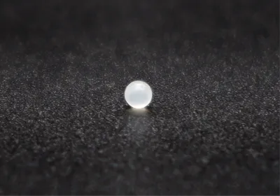 A fat-absorbing microbead, white and pearl-like, lies on a black speckled surface.