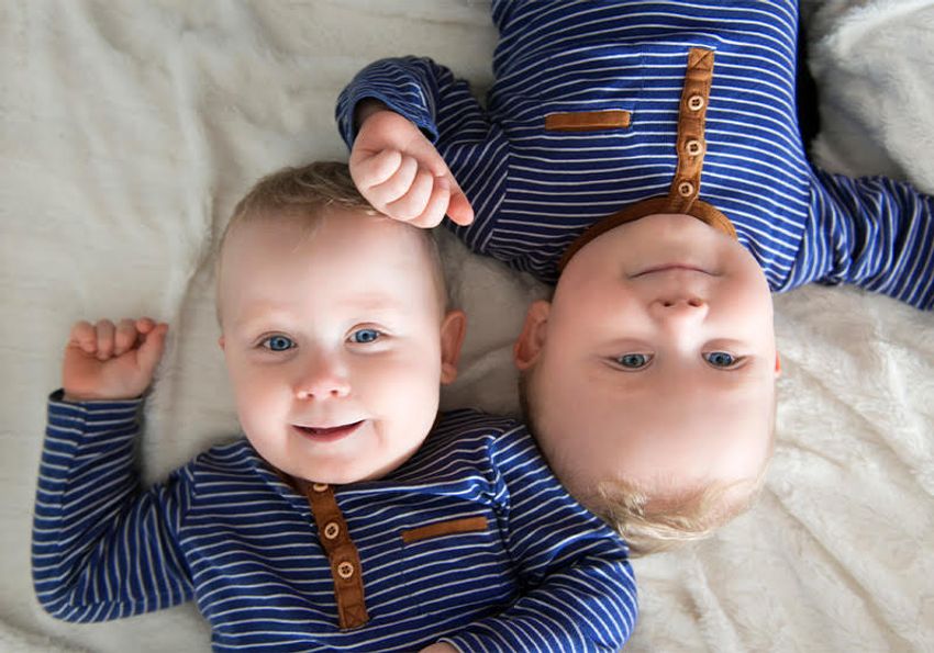 A pair of identical twins lie opposite from each other on a white blanket. A pair of identical twins lie opposite from each other on a white blanket.