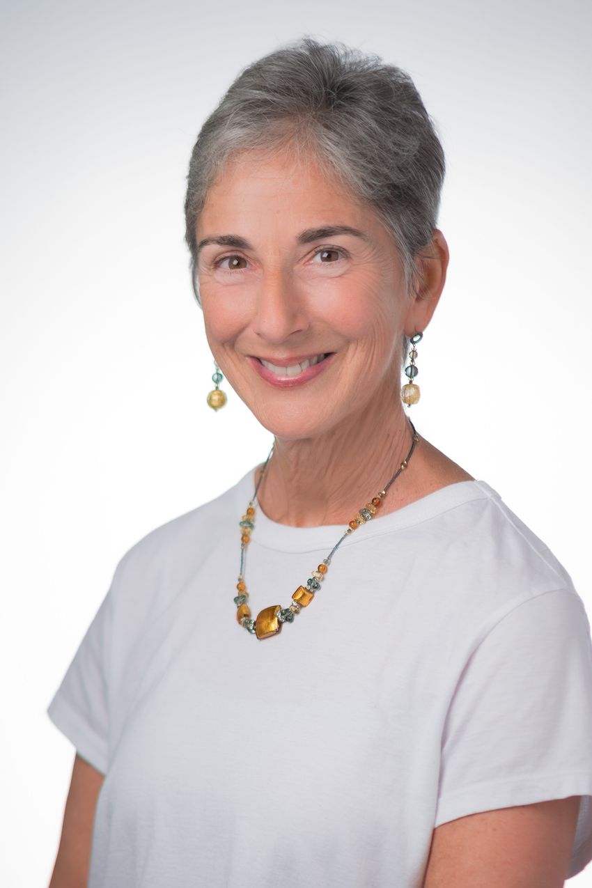 Jennifer Grandis, wearing a white T-shirt and matching bead earrings and necklace, poses in front of a white background.