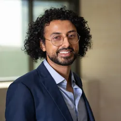 A photograph of Manoj Doss wearing a blue shirt and navy blue blazer. A photograph of Manoj Doss wearing a blue shirt and navy blue blazer.