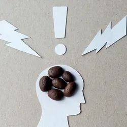 Image of a cutout silhouette of a person’s profile with six coffee beans clustered in their head. There are cutout shapes of two lightning bolts and an exclamation point above their head. Image of a cutout silhouette of a person’s profile with six coffee beans clustered in their head. There are cutout shapes of two lightning bolts and an exclamation point above their head.