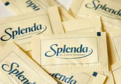Light yellow packets of Splenda, a common trade name for sucralose and the artificial sweetener recently found to worsen response to cancer immunotherapy, are strewn all over a white surface.