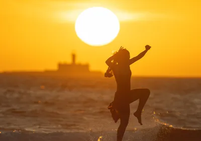 A woman leaps joyfully with the sun in the background, signifying the link between sunlight and happiness. A woman leaps joyfully with the sun in the background, signifying the link between sunlight and happiness.