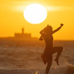A woman leaps joyfully with the sun in the background, signifying the link between sunlight and happiness.